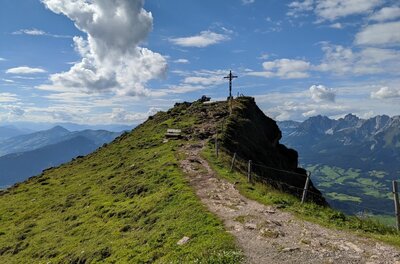 Horn Gipfel-Höhenweg Schmaler Wanderweg führt über einen grasbewachsenen Grat zu einem Gipfelkreuz unter blauem Himmel.