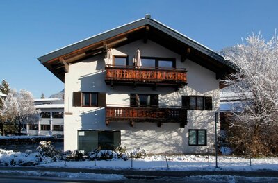 Winteransicht Appartement Elisabeth Alpines Wohnhaus mit Holzbalkonen im Schnee unter blauem Himmel.