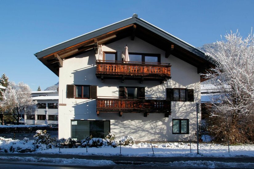 Alpines Wohnhaus mit Holzbalkonen im Schnee unter blauem Himmel.