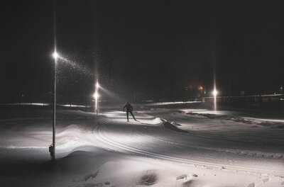 Person beim Skilanglauf auf einer beleuchteten Nachtloipe bei Dunkelheit.