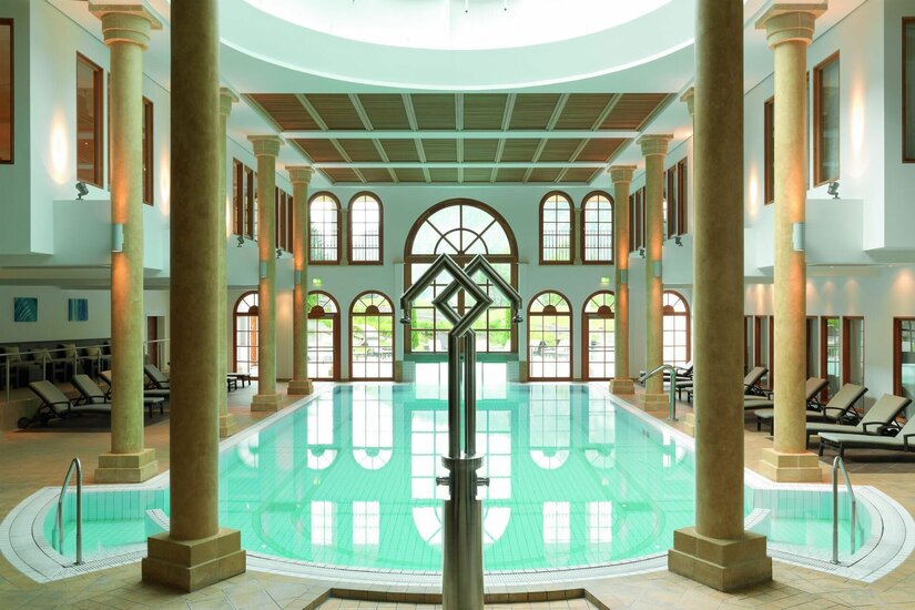 SPA-ROSA Innenpool Hallenbad mit Säulen, Liegestühlen und großen Rundbogenfenstern.