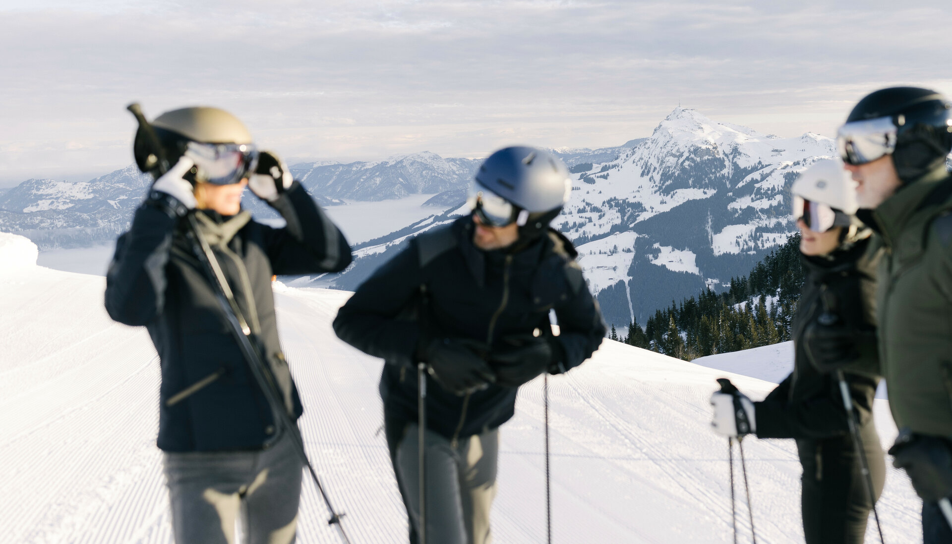 Eine Gruppe von Skifahrern steht auf einer schneebedeckten Piste im Skigebiet Kitzbühel und bereitet sich auf die Abfahrt vor, umgeben von Bergen.