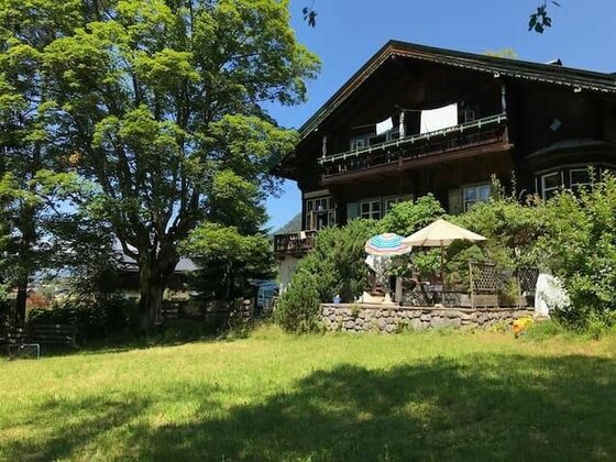 Villa Momo - Sommerfrische Dunkles Holzhaus mit Balkon, Terrasse und Garten unter blauem Himmel.