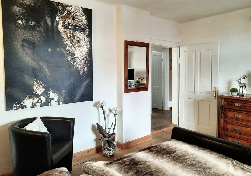 Schlafzimmer mit großem Porträtgemälde, Ledersessel, Holzboden und einer Kommode.
