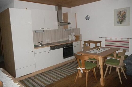 Moderne Küchenzeile mit weißen Fronten und angrenzendem Holzesstisch mit Stühlen.