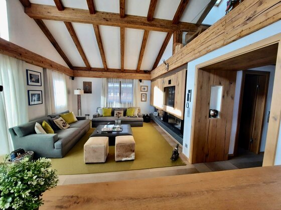 Moderner Wohnraum mit grauen Sofas, Holzbalkendecke und einem großen Teppich unter einem Couchtisch.