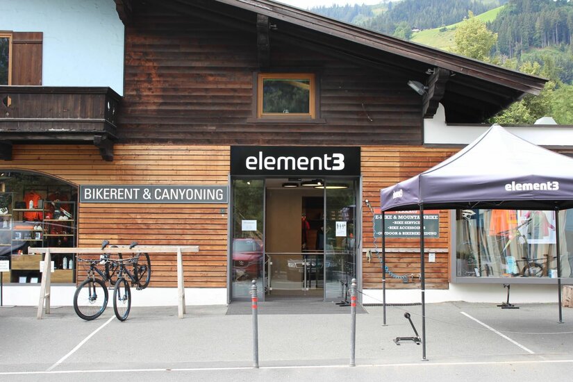 Element3 Adventure Center Eingangsbereich eines Sportgeschäfts mit Holzfassade, Fahrrädern im Ständer und einem schwarzen Zeltdach.