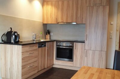 Küche der Wohnung EG1 Moderne Einbauküche in L-Form mit hellen Holzfronten, Backofen, Ceranfeld und Kaffeemaschine.
