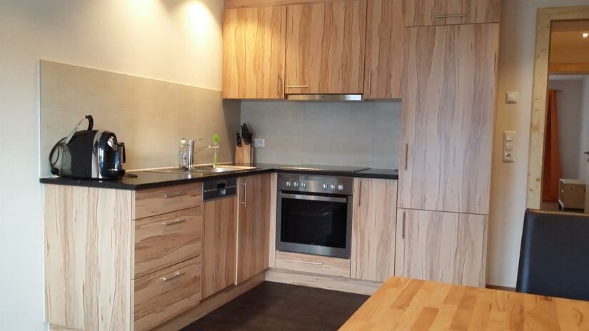 Moderne Einbauküche in L-Form mit hellen Holzfronten, Backofen, Ceranfeld und Kaffeemaschine.