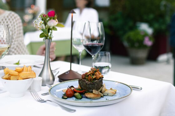 Kulinarik im Hotel Kaiserhof Ein angerichteter Teller mit Steak, Pilzen und Gemüse auf einem weiß gedeckten Restauranttisch im Freien.