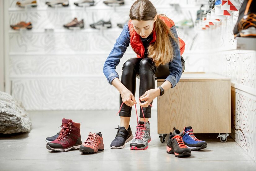 Schuhberatung bei Kitzsport Pepi Eine Frau sitzt in einem Sportgeschäft und schnürt einen grauen Wanderschuh mit pinken Akzenten.