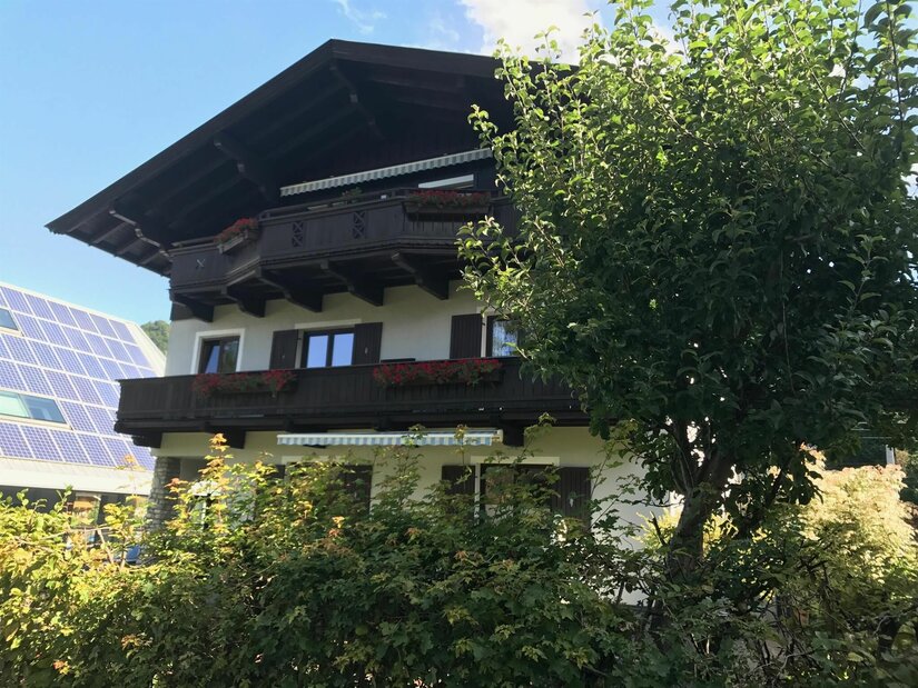 Haus Pankratz Mehrstöckiges Alpenhaus mit dunklen Holzbalkonen, Blumenkästen und Photovoltaikanlage im Hintergrund.