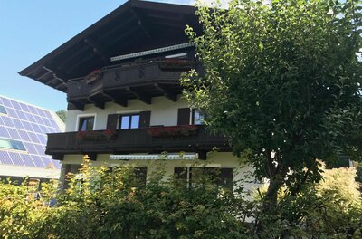 Mehrstöckiges Alpenhaus mit dunklen Holzbalkonen, Blumenkästen und Photovoltaikanlage im Hintergrund.