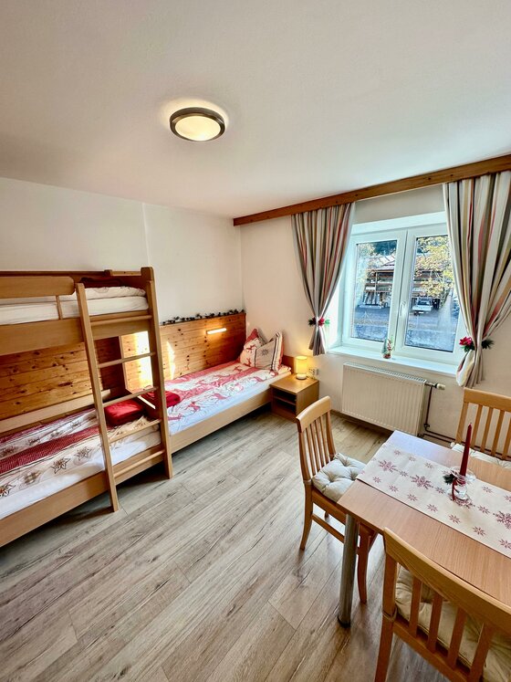 Zimmer in Central Kitz Apartments Helles Zimmer mit Holz-Etagenbett, Einzelbett, Esstisch und Fenster.