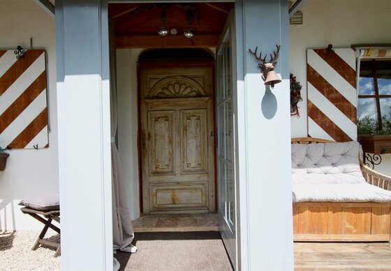 Eingangsbereich eines Chalets mit verzierter Holztür, rot-weiß gestreiften Fensterläden und einer Holzbank.