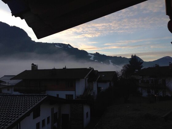 Blick über Hausdächer auf nebelverhangene Berge bei Dämmerung.