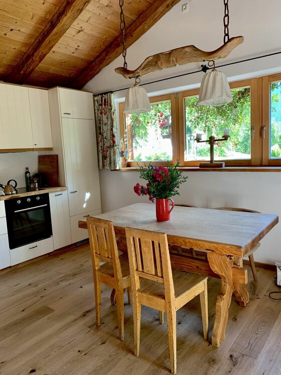 Küche im Zuhaus Schernfeichten Rustikale Holzküche mit Esstisch, Stühlen und Blick aus dem Fenster auf Bäume.