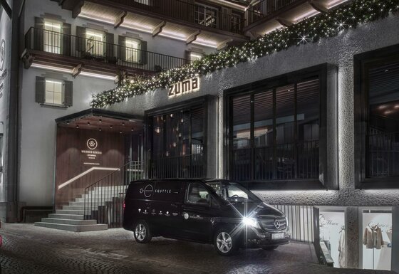 Außenansicht des Hotels Weisses Rössl in Kitzbühel bei Nacht mit einem schwarzen Shuttle-Bus davor.