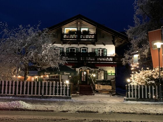 Hotel Villa Licht bei Nacht Beleuchtetes alpines Hotelgebäude bei Nacht mit verschneitem Vorplatz und Holzzaun.
