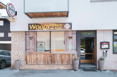 Außenansicht der Woody's Stadl Bar mit Holzverkleidung, Herz-Ausschnitten und Firmenschild.