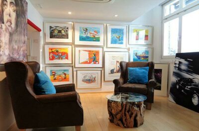 Walentowski Galerie Kitzbühel Eine gemütliche Sitzecke mit zwei Stühlen und einem Glastisch. An der Wand hängen farbenfrohe Kunstwerke in Rahmen.