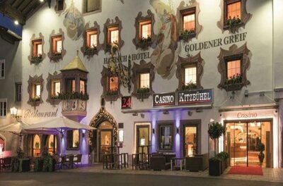 Ein traditionelles Hotelgebäude mit bunten Fenstern und schöner Fassade. Im Vordergrund ist ein Casino und Außensitzplätze sichtbar.