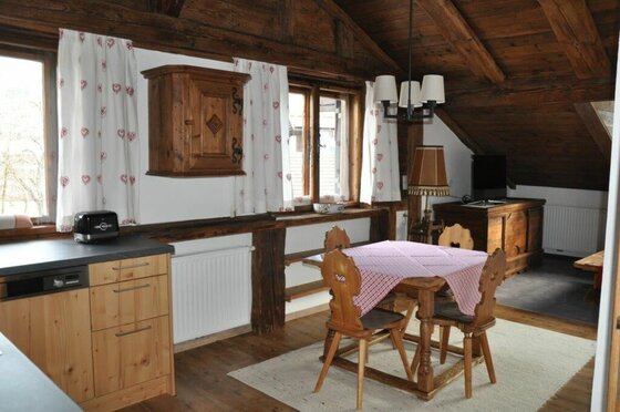 Rustikaler Essbereich mit Holztisch, Stühlen und Küchenzeile unter einer Dachschräge aus Holz.