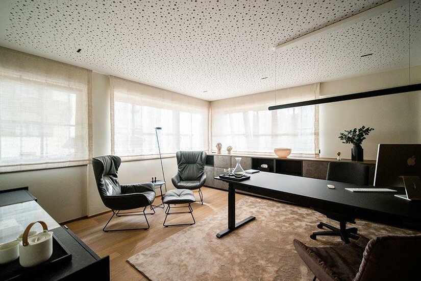 Modernes Büro mit Schreibtisch, zwei Ledersesseln und einer perforierten Decke.