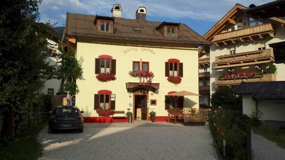 Pension Johanna in Kitzbühel Zweistöckiges gelbes Gebäude der Pension Johanna mit Blumenkästen vor den Fenstern und einem Kiesparkplatz davor.