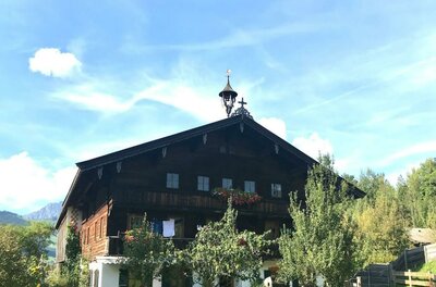 Seebachhof Ein traditionelles Holzhaus mit einem spitzen Dach und einem kleinen Turm. Umgeben von Bäumen und einem klaren Himmel.
