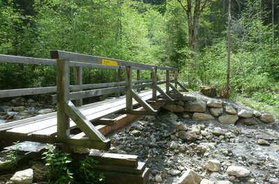 Schleierwasserfall Eine Holzkonstruktion über einen kleinen Bach, umgeben von grünen Bäumen. Der Weg lädt zu einem ruhigen Spaziergang in der Natur ein.