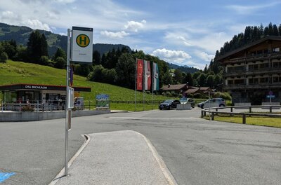 Bushaltestellenschild vor einem Parkplatz mit Bergen im Hintergrund.