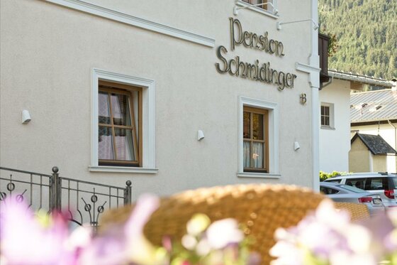 Außenansicht der Pension Schmidinger mit Schriftzug an der hellen Hauswand und Fenstern.