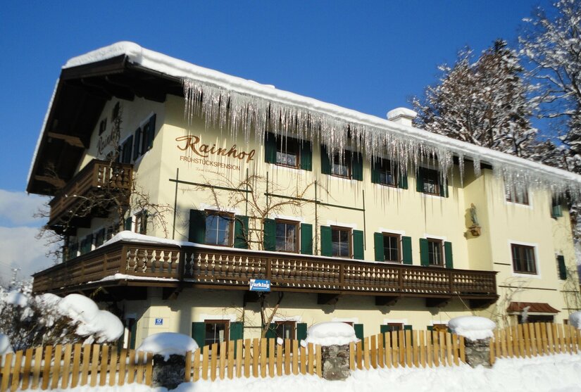 Gelbes Pensionsgebäude mit schneebedecktem Dach und langen Eiszapfen an der Dachrinne.