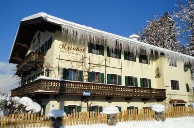 Gelbes Pensionsgebäude mit schneebedecktem Dach und langen Eiszapfen an der Dachrinne.