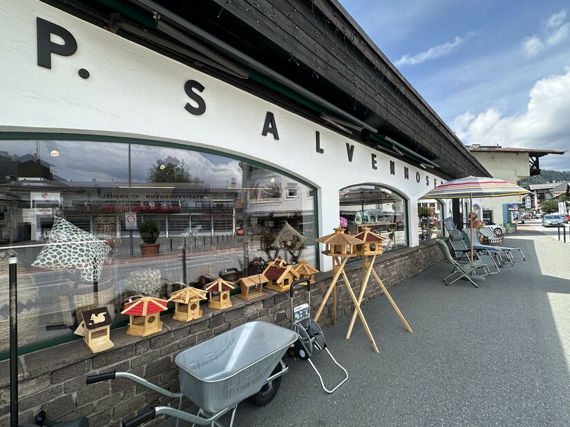Außenansicht des Geschäfts Salvenmoser mit Vogelhäusern, Schubkarre und Gartenmöbeln vor dem Schaufenster.