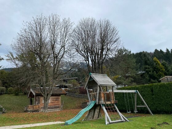 Spielplatz beim Hotel Vordergrub Kinderspielplatz aus Holz mit Rutsche, Klettergerüst und Schaukel vor Bäumen.