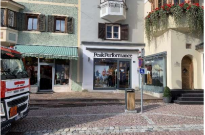 Ein Einkaufsgeschäft mit dem Namen "Peak Performance" ist sichtbar. Daneben befinden sich weitere Läden und eine gepflasterte Straße.