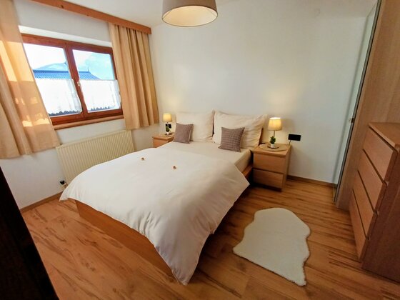 Ein gemütliches Schlafzimmer mit einem Doppelbett und zwei Nachttischen. Die hellen Vorhänge und das Holzfußboden sorgen für eine warme Atmosphäre.
