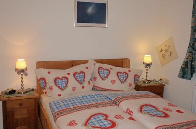 Ein gemütliches Schlafzimmer mit einem Doppelbett und Bettwäsche in Herzdesign. An den Nachttischen stehen kleine Lampen, und an der Wand hängt ein Bild.