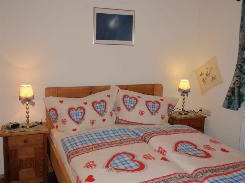 Schlafzimmer Ein gemütliches Schlafzimmer mit einem Doppelbett und Bettwäsche in Herzdesign. An den Nachttischen stehen kleine Lampen, und an der Wand hängt ein Bild.