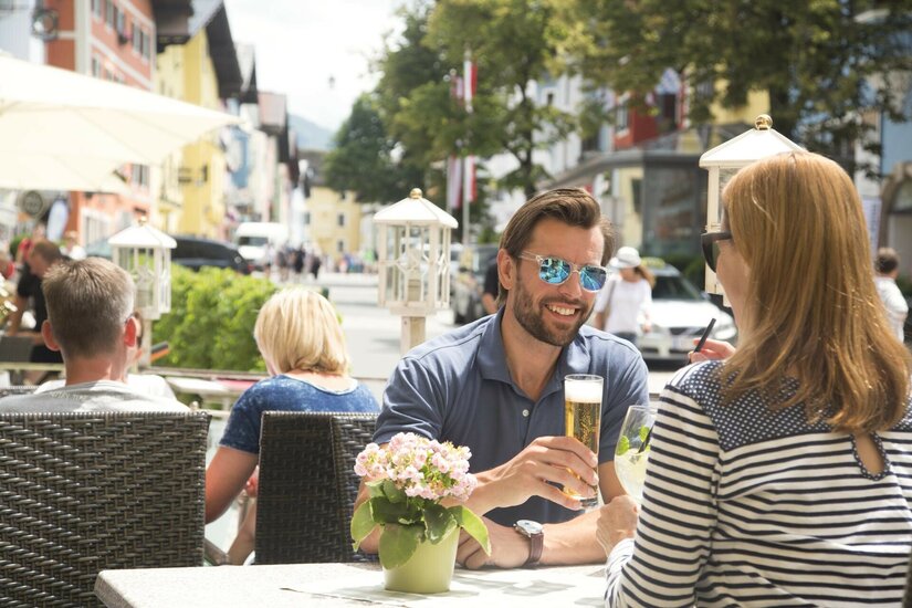 Gastgarten Goldene Gams Ein Mann und eine Frau sitzen an einem Tisch im Außenbereich eines Cafés in einer belebten Fußgängerzone.