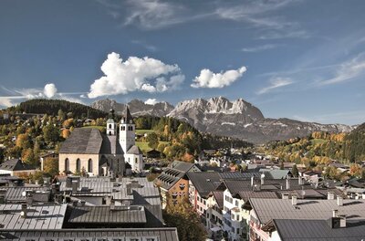 Blick über die Dächer von Kitzbühel mit der Stadtpfarrkirche und dem Wilden Kaiser im Hintergrund.
