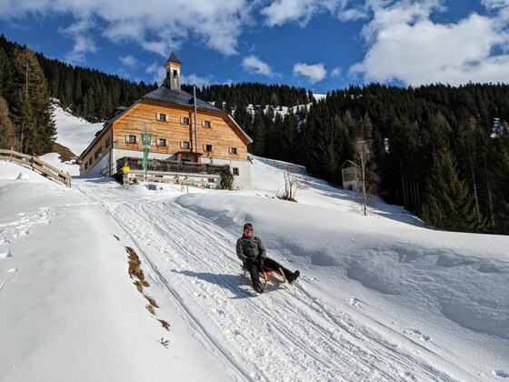 Person fährt auf einem Holzschlitten eine verschneite Bahn vor der Kelchalm hinunter.