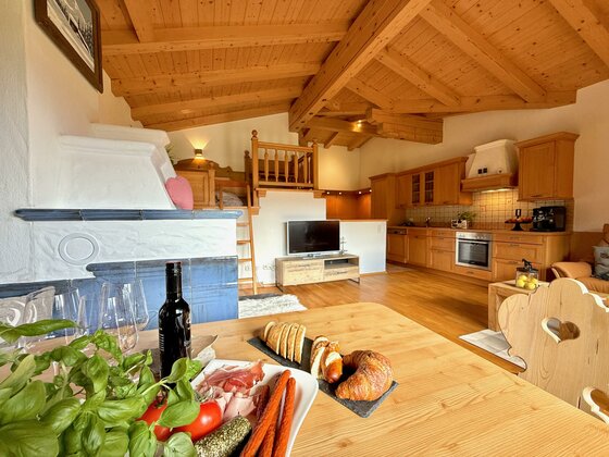 Eine gemütliche Wohnung mit Holzbalken und modernen Küchenelementen. Auf dem Tisch liegen frische Lebensmittel und ein Flasche Wein.