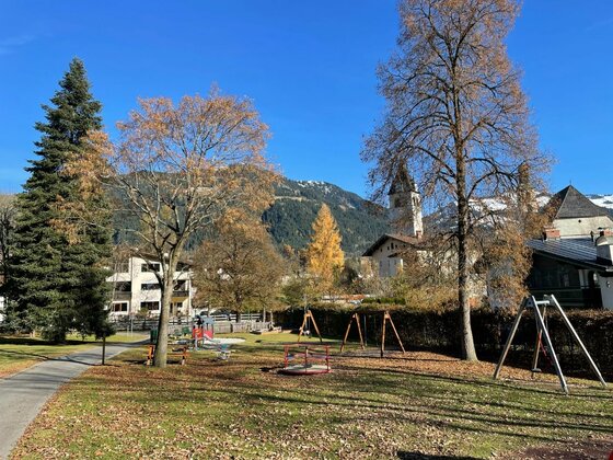 Spielplatz Pfarrau im Herbst Ein öffentlicher Spielplatz mit Schaukeln und Karussell vor einer Bergkulisse im Herbst.