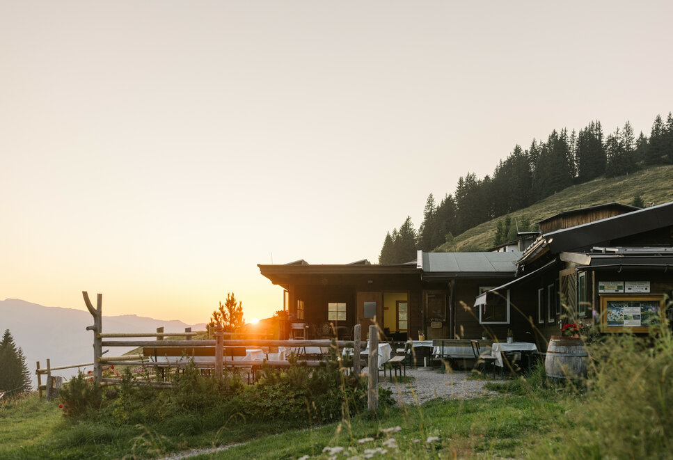 Ein charmantes Holzhaus in den Alpen, umgeben von Natur, während die letzten Sonnenstrahlen den Tag verabschieden.