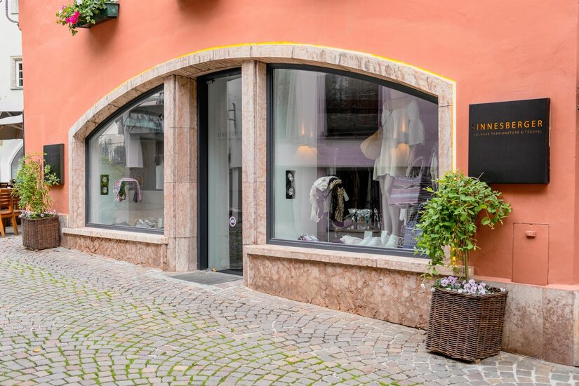 Sinnesberger Fashionstore Kitzbühel Außenansicht des Sinnesberger Fashionstores mit Schaufenstern in einer gepflasterten Gasse.
