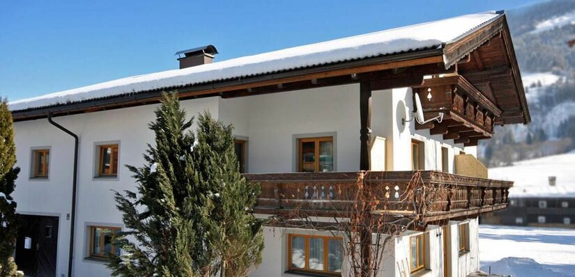 Zweistöckiges weißes Gästehaus mit Holzbalkonen und schneebedecktem Dach in einer Winterlandschaft.