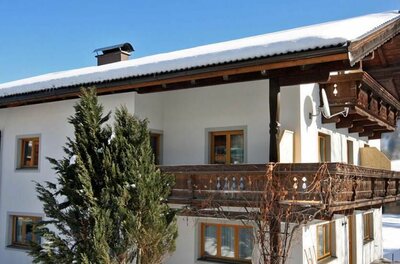 Zweistöckiges weißes Gästehaus mit Holzbalkonen und schneebedecktem Dach in einer Winterlandschaft.
